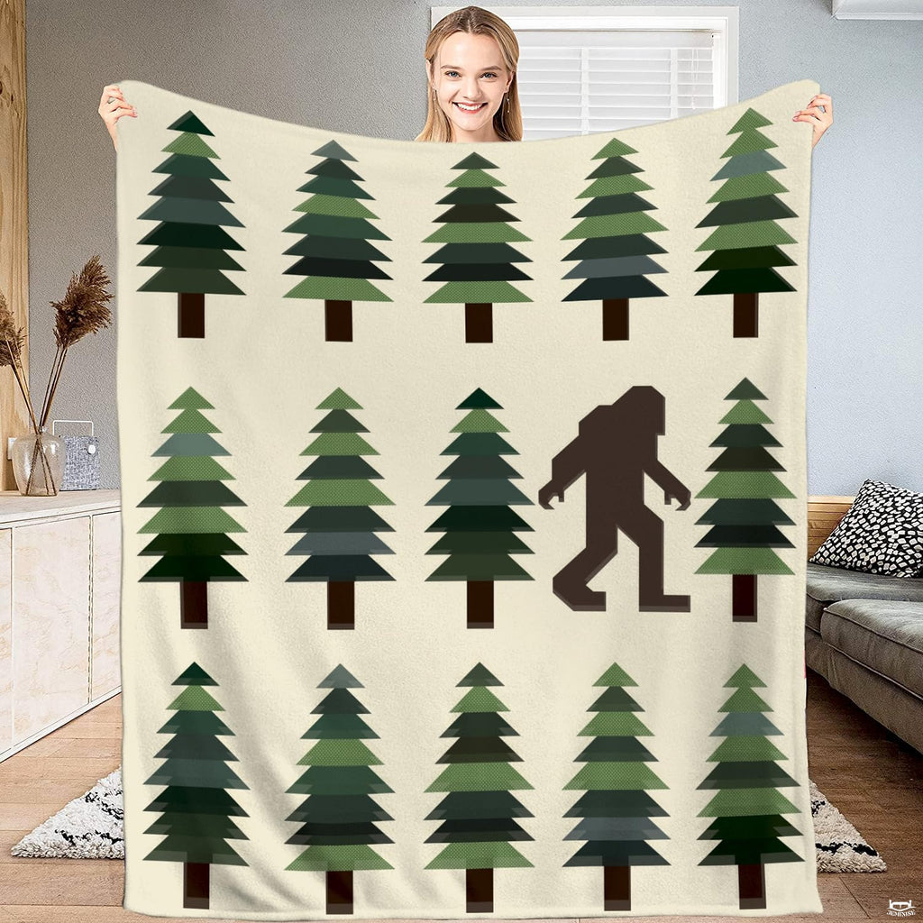 Bigfoot blanket held open showing geometric pine trees and walking Sasquatch silhouette on cream background.