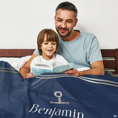Parent and child reading a book in bed draped in the navy blue anchor print.