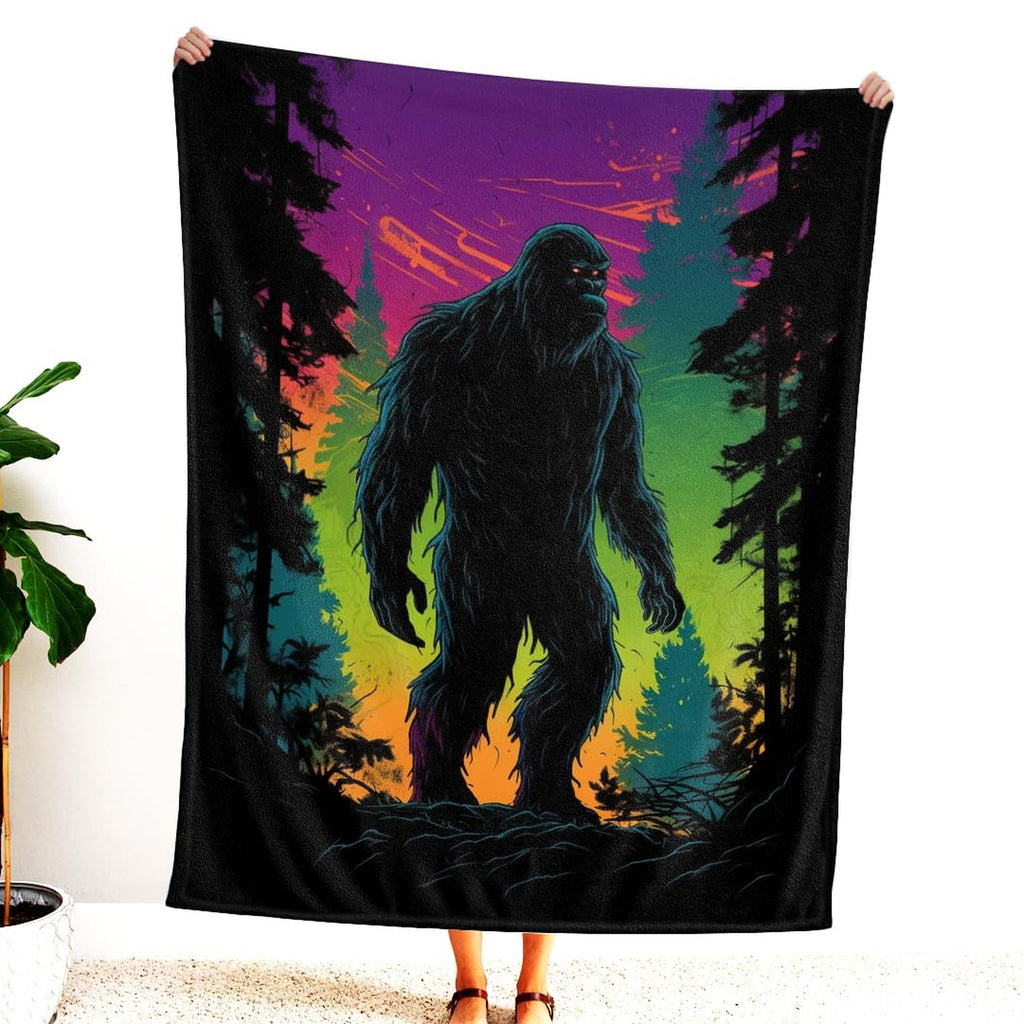 Person holding up the blanket displaying the neon Bigfoot silhouette and vibrant sunset sky.