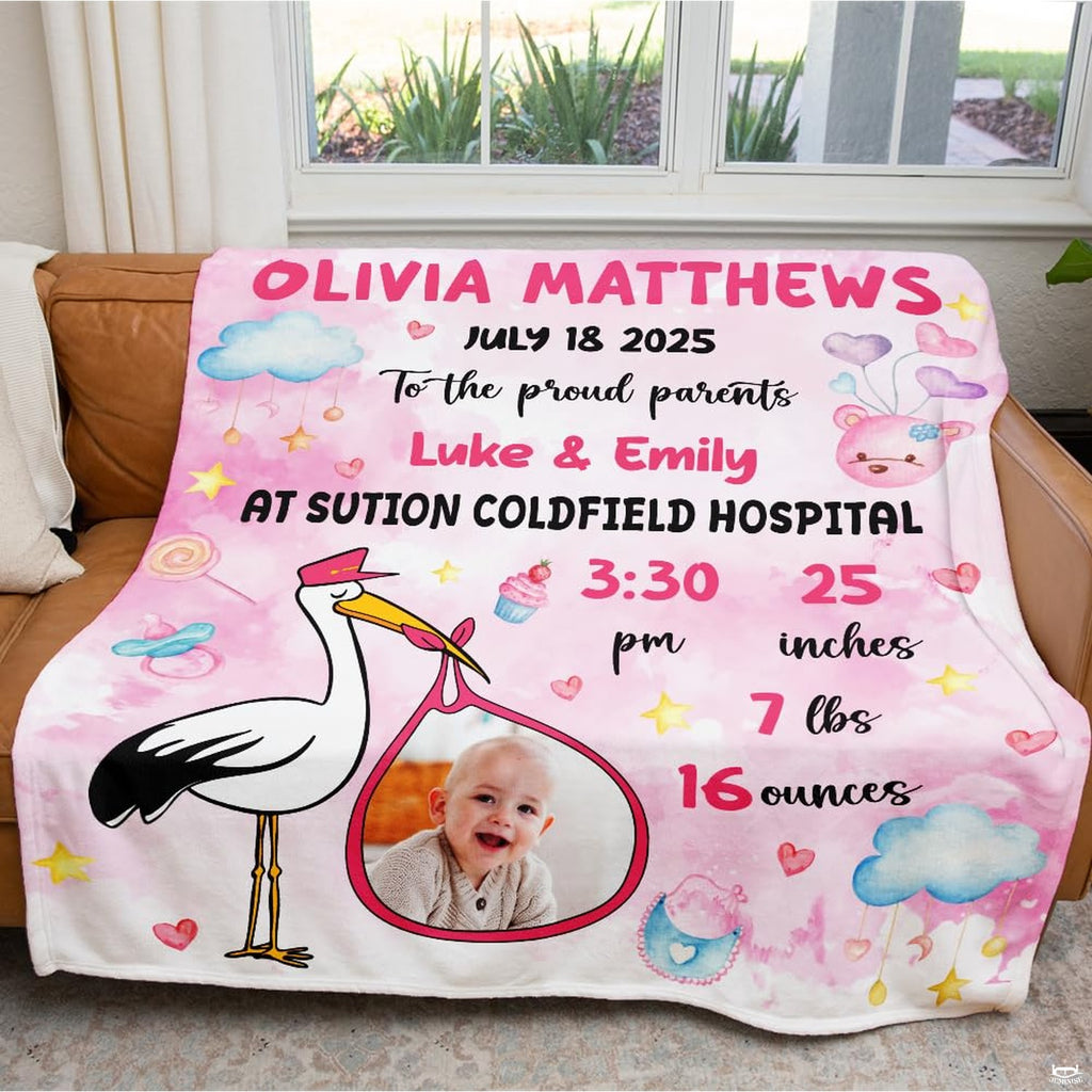 Blush pink watercolor stork milestone blanket draped across a living room leather sofa.