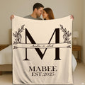 Botanical split initial throw blanket with laurel leaves and arrow crest on cream