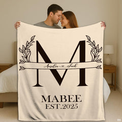 Botanical split initial throw blanket with laurel leaves and arrow crest on cream
