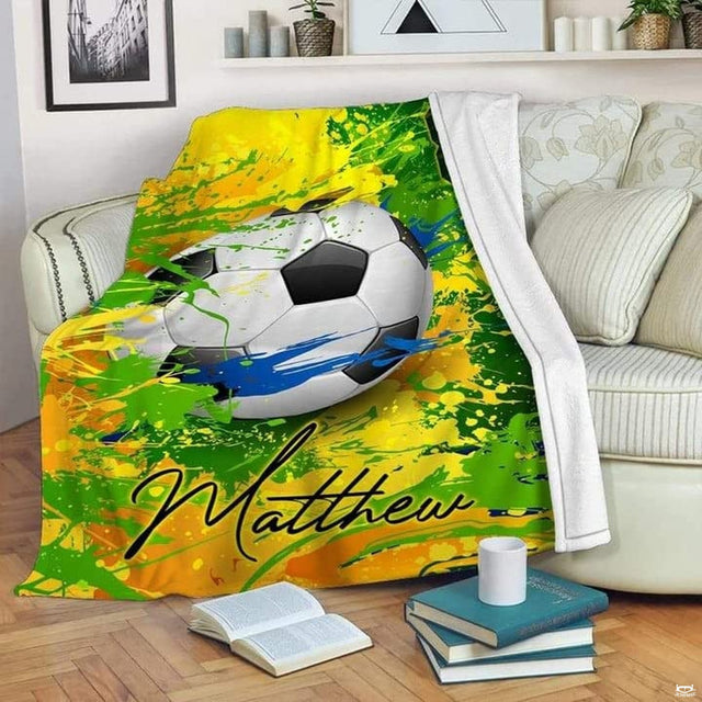 Soccer paint splatter blanket featuring soccer ball surrounded by vibrant green, yellow, and blue paint drips.