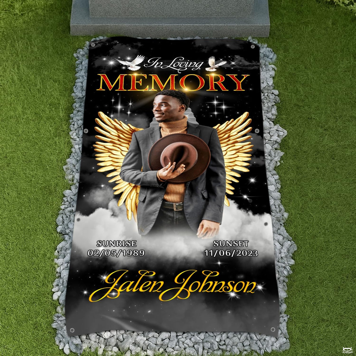Memorial blanket tribute displayed on a cemetery lawn surrounded by decorative white river stones.