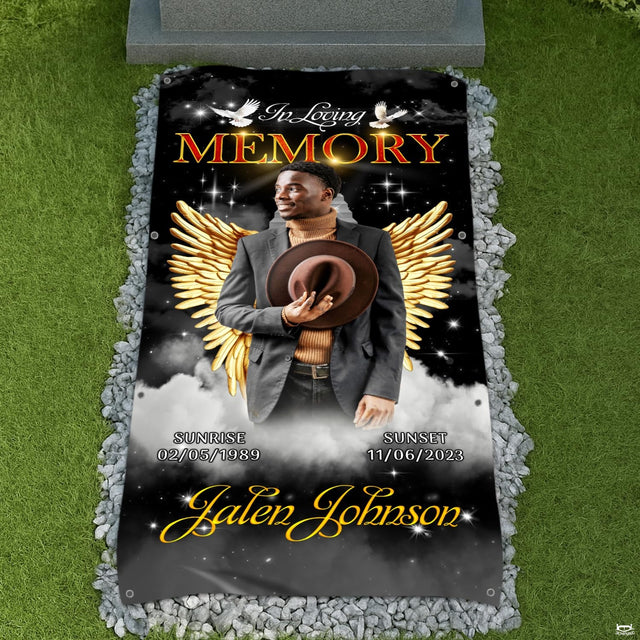 Memorial blanket tribute displayed on a cemetery lawn surrounded by decorative white river stones.