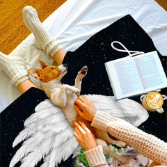 Black angel wings throw blanket draped over bedding beside a puppy and open book