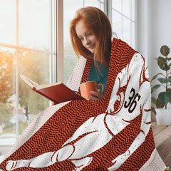 Woman wrapped comfortably in football throw blanket while reading a book near a sunny window.