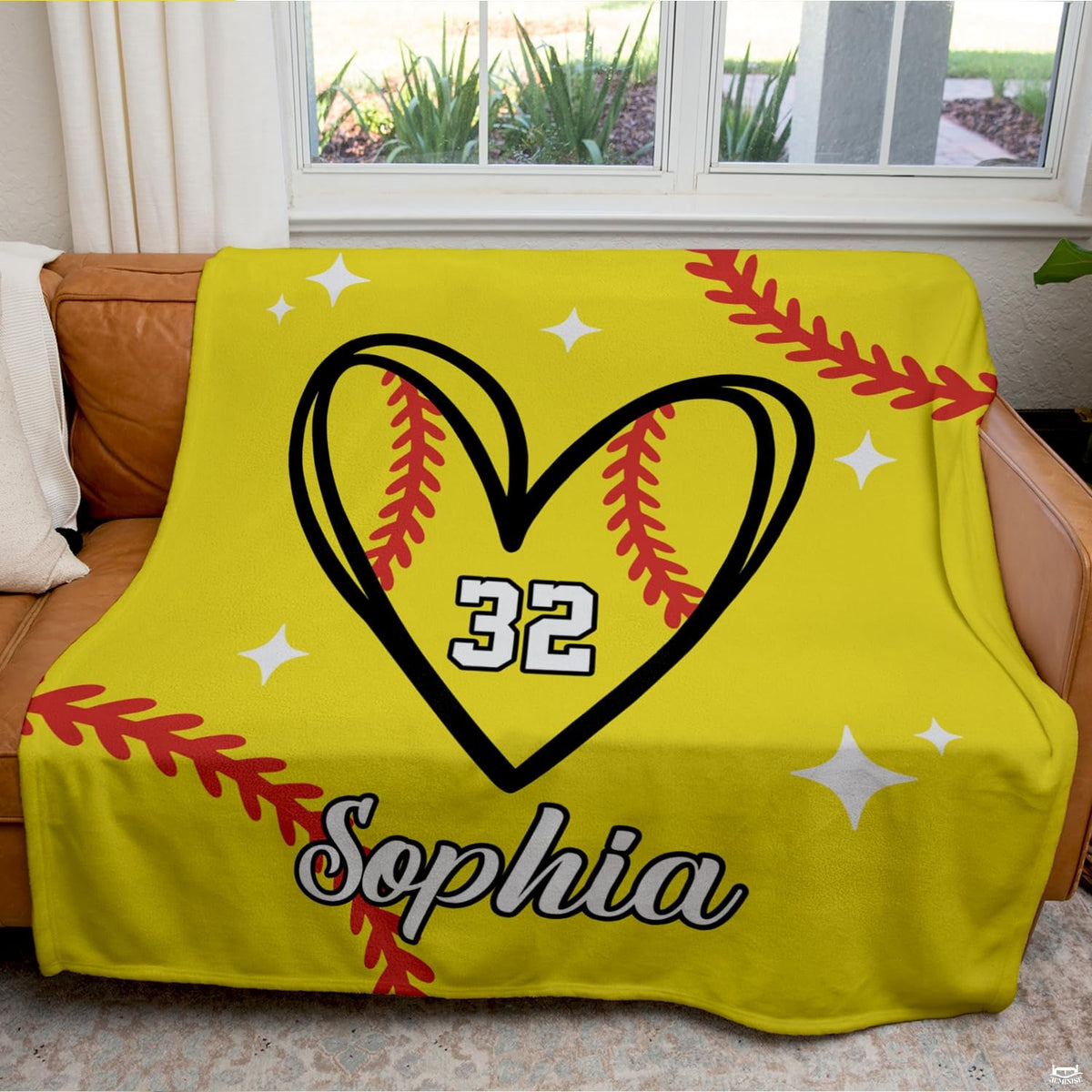 Living room staging displaying softball heart throw blanket styled across a modern sofa.